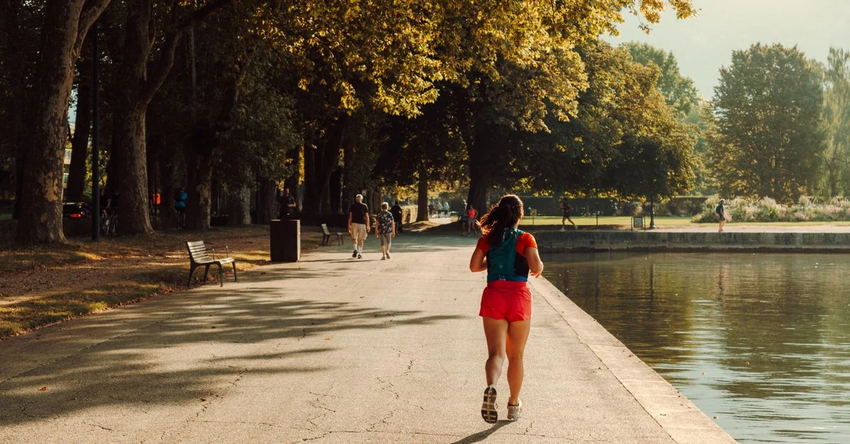 Une femme courant dans un parc vibrant près de l'eau, illustrant une journée ensoleillée.