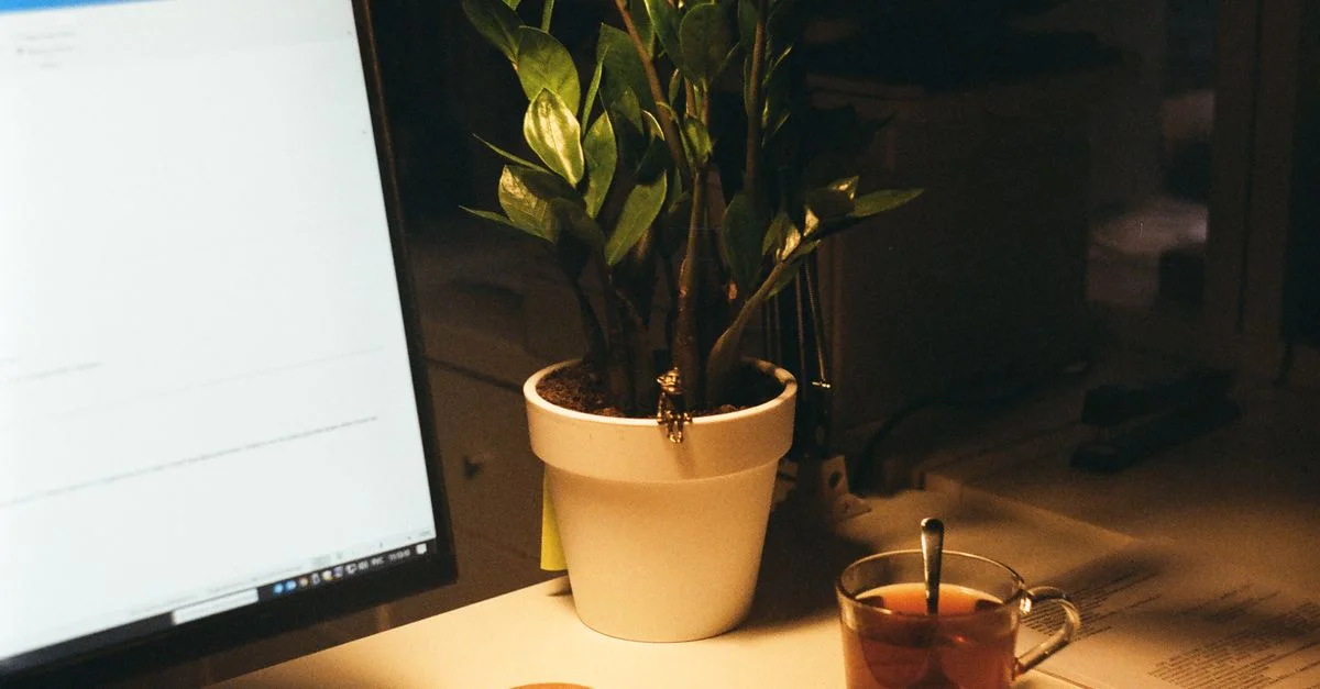 Un espace de travail chaleureux et accueillant avec un écran d'ordinateur, une plante en pot et une tasse de thé.