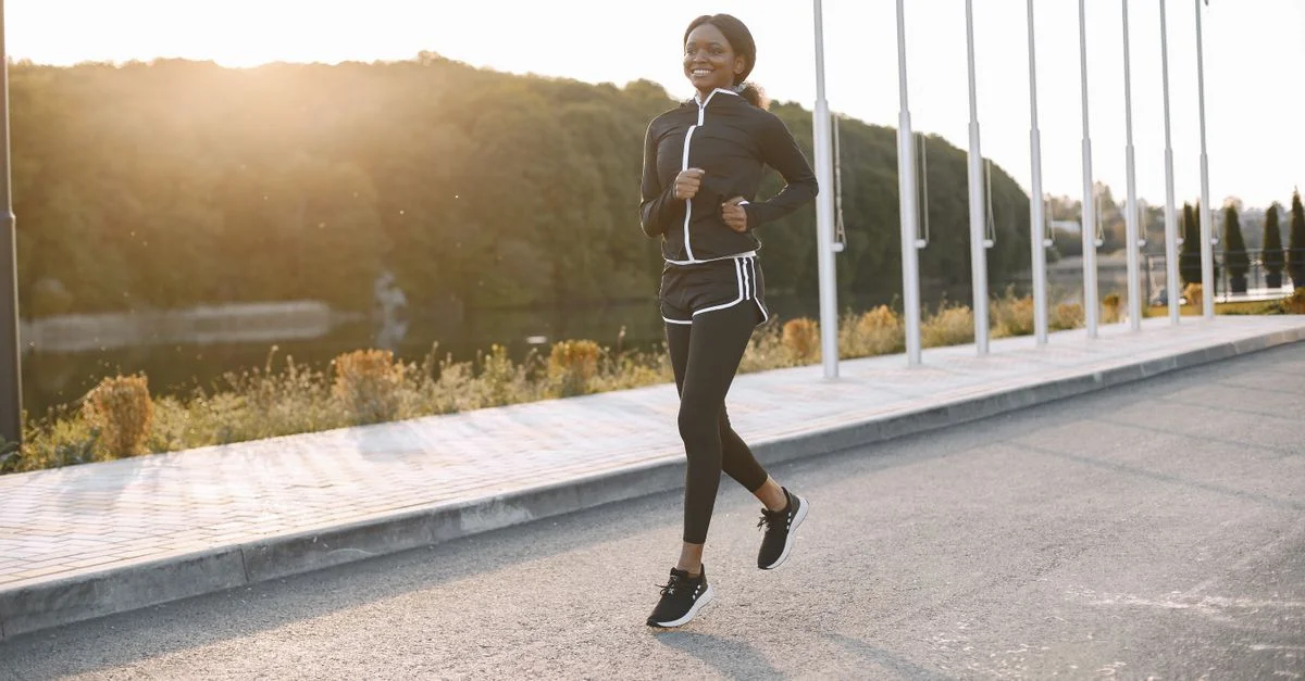 Une femme courant sur un chemin ensoleillé, mettant en avant le fitness et le sport.