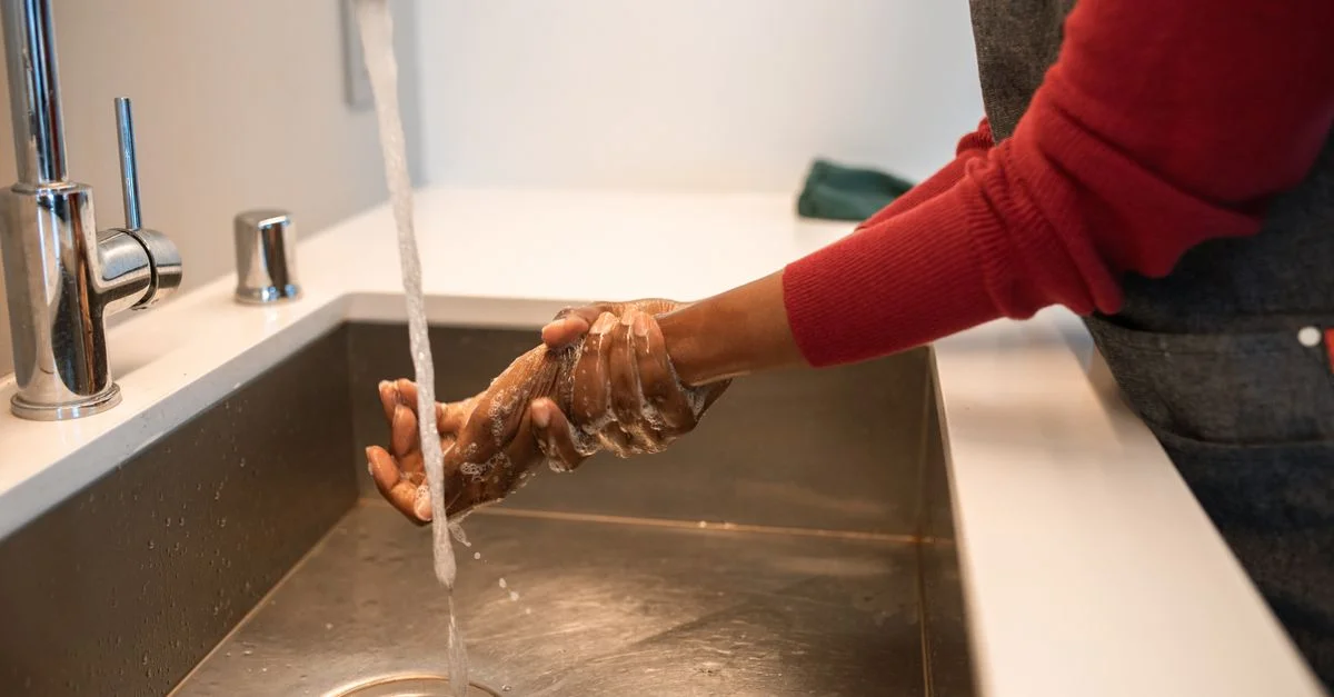 Gros plan sur des mains lavées sous un robinet en acier inoxydable avec de l'eau courante.